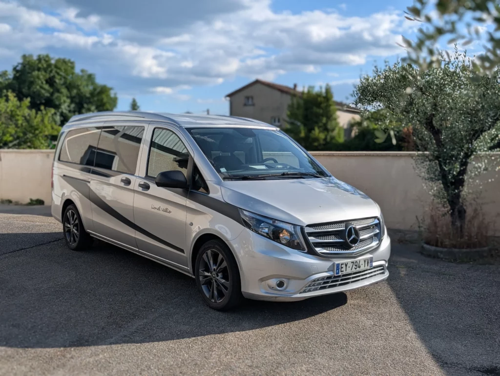 Corbillard van Mercedes gris métallisé stationné devant l'agence.