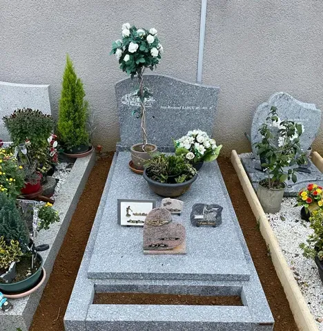 Monument funéraire en granit gris fleuri avec plaques commémoratives.