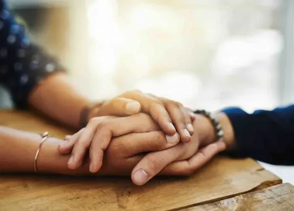 Mains enlacées sur une table en bois symbolisant le soutien et le deuil.
